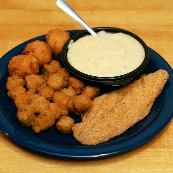 A fried catfish fillet, hushpuppies, fried okra, and a bowl of grits on a blue plate.