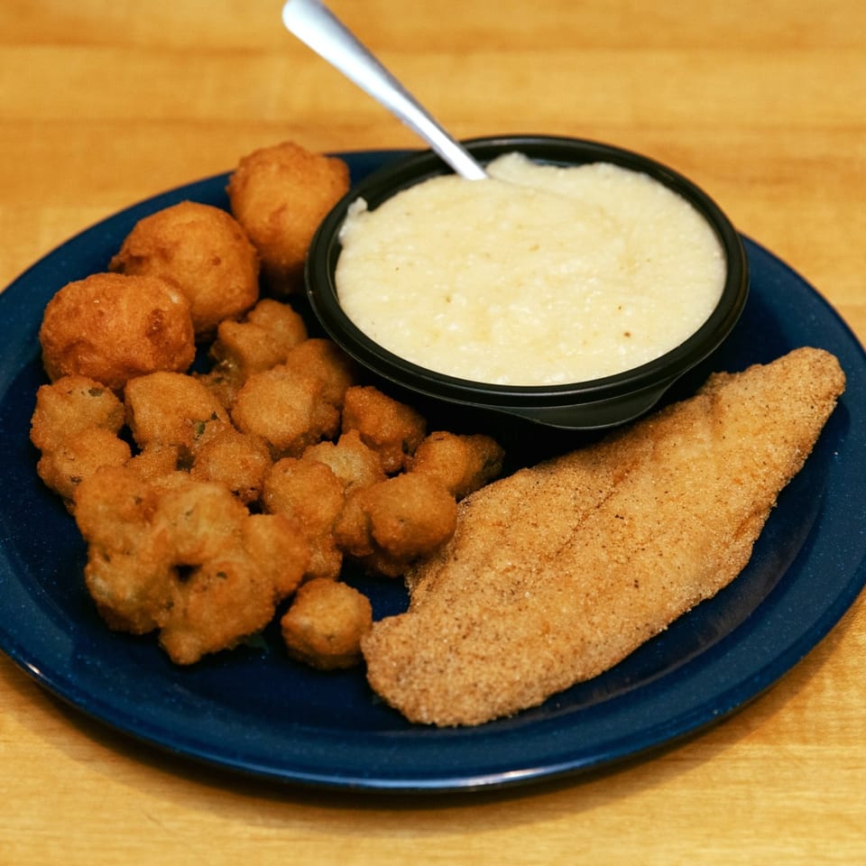 A fried catfish fillet, hushpuppies, fried okra, and a bowl of grits on a blue plate.
