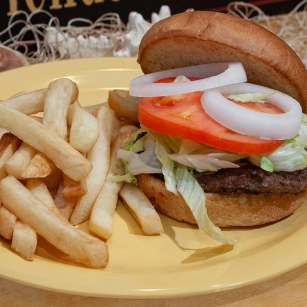 A burger with lettuce, tomato, and onion, served with a side of french fries on a yellow plate.